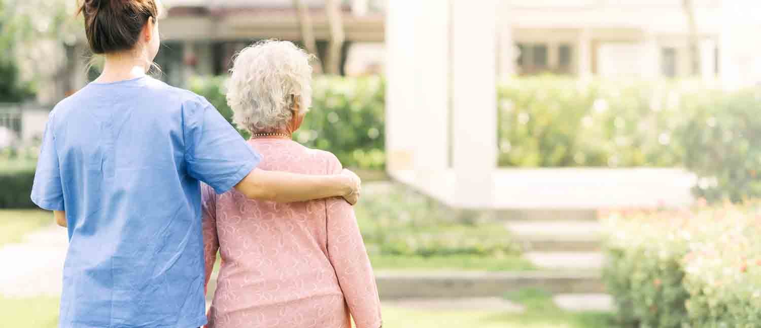 Back view of nurse caregiver support walking with elderly woman outdoor